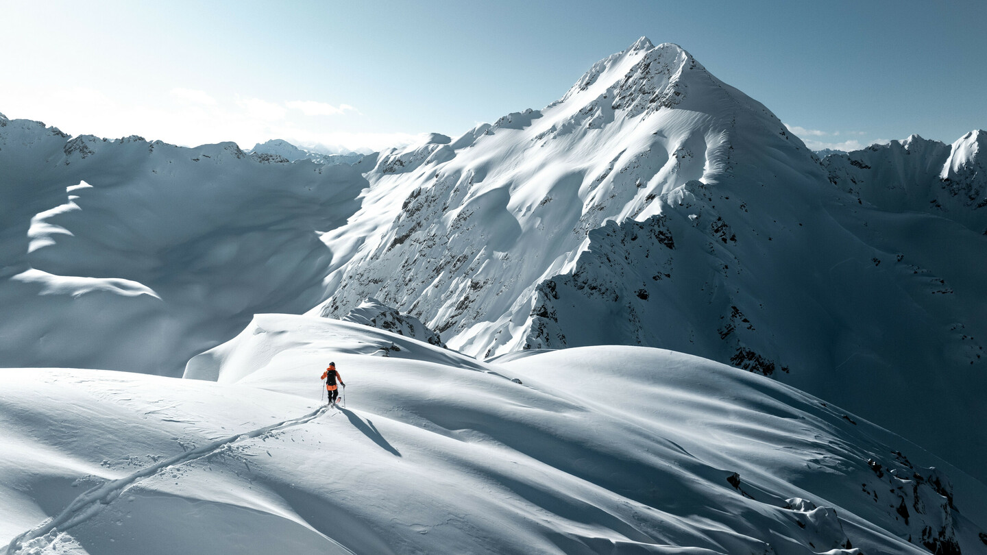 Ein Skifahrer auf einer verschneiten Berglandschaft bei Sonnenschein, umgeben von majestätischen Gipfeln und unberührtem Schnee.